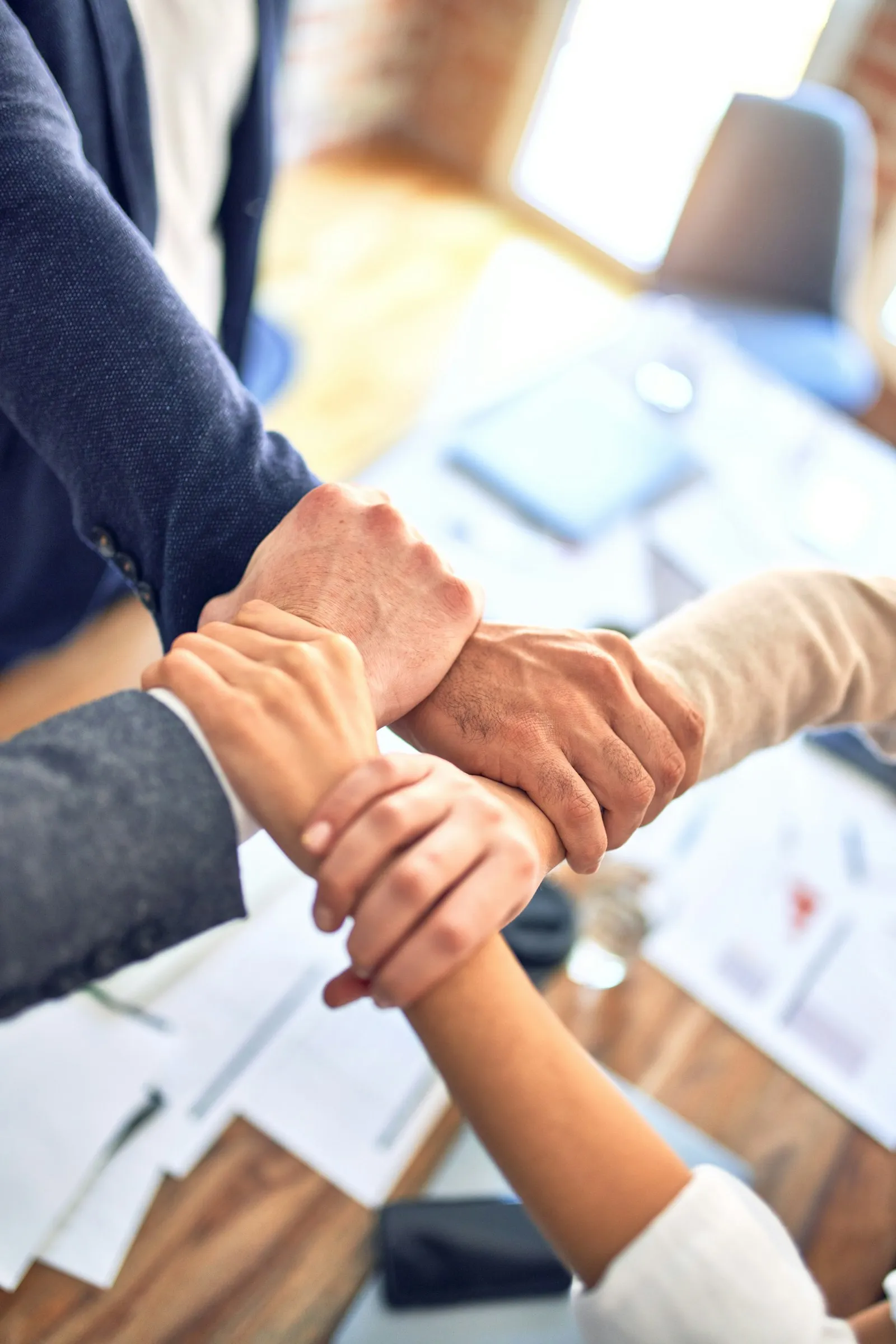 Dua tangan bergenggaman di atas meja kerja penuh catatan, melambangkan kesepakatan jadwal pengerjaan keramik